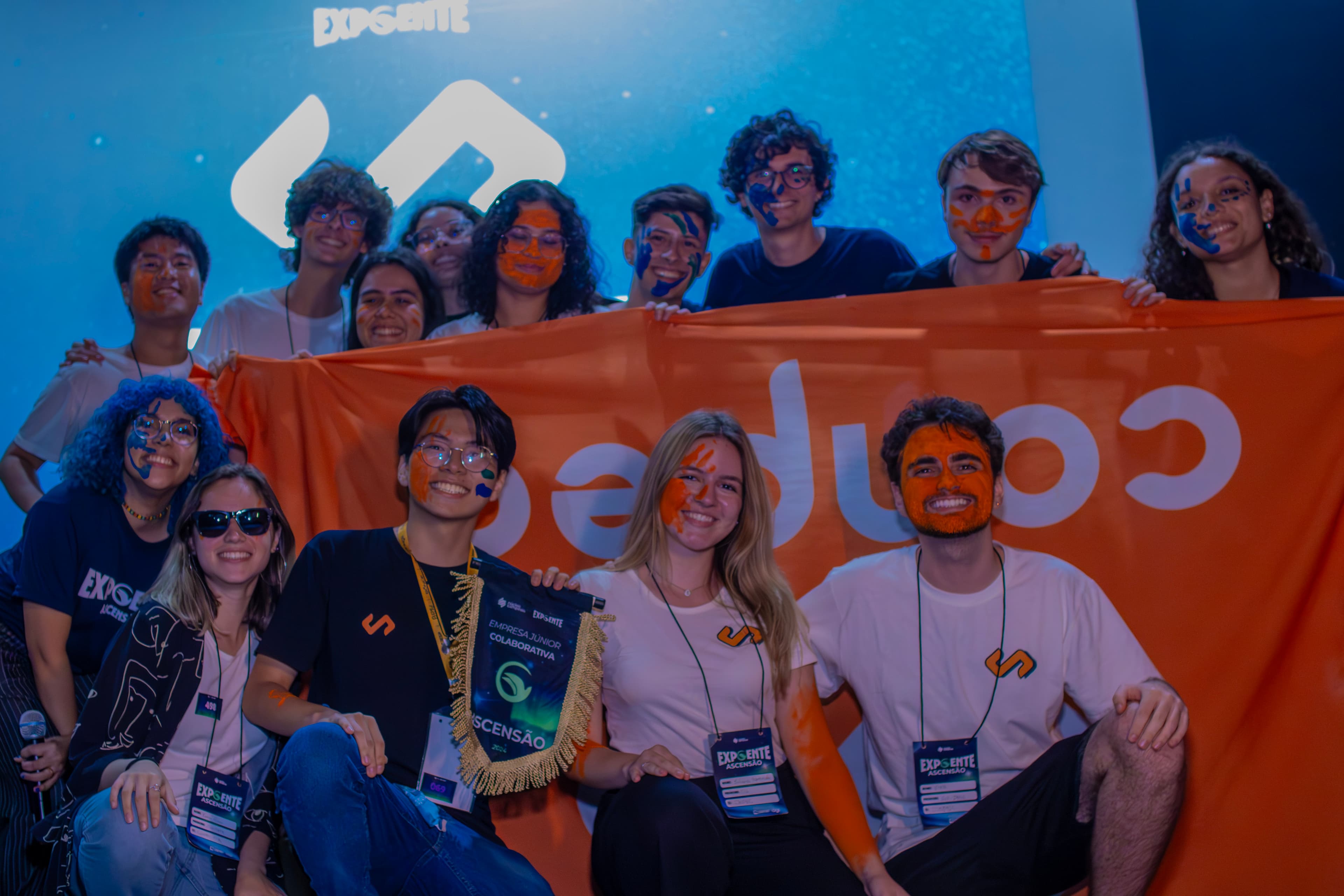 Três pessoas olham sorrindo para a câmera. Uma delas está usando um chapéu laranja, escrito "Fica de boa".