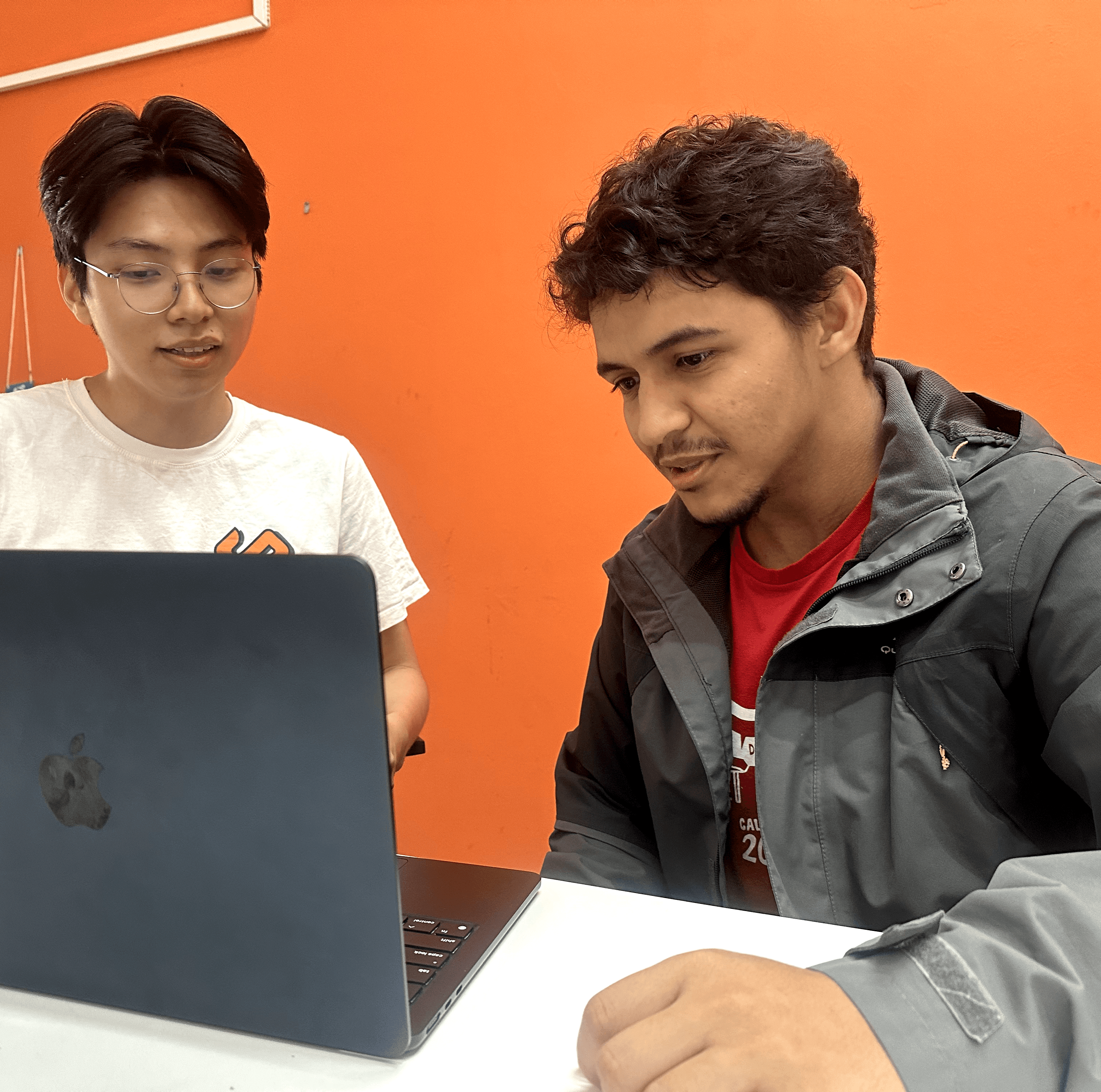 Dois homens, usando a camisa da Conpec, discutem em frente à um computador.